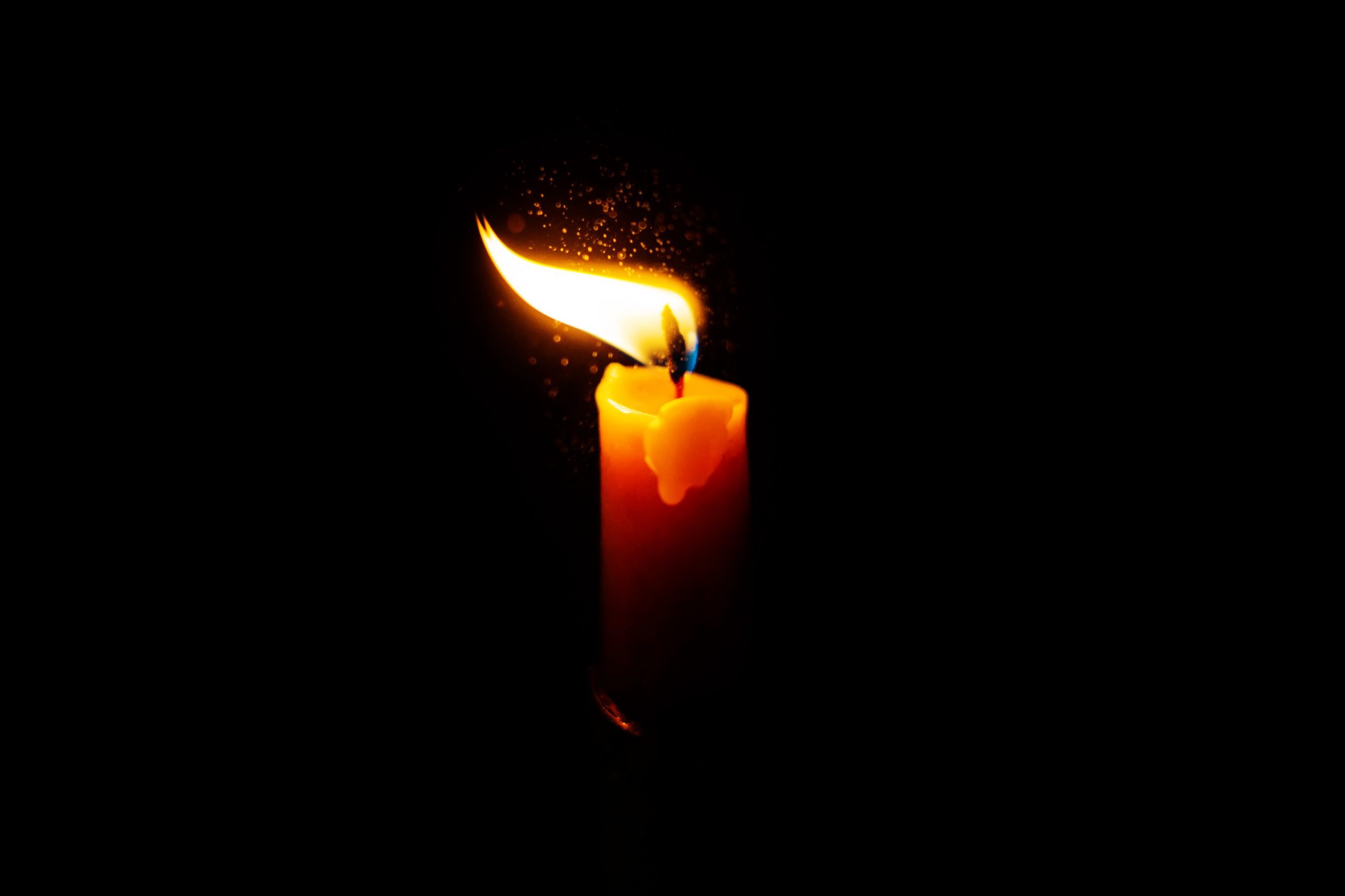 A bright candle burns in the darkness, sparks flying. A candle in memory of the deceased. Sadness and sorrow.